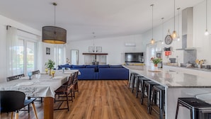 Una cocina moderna con una isla central, un comedor con una mesa larga y un sofá azul en la sala de estar.
