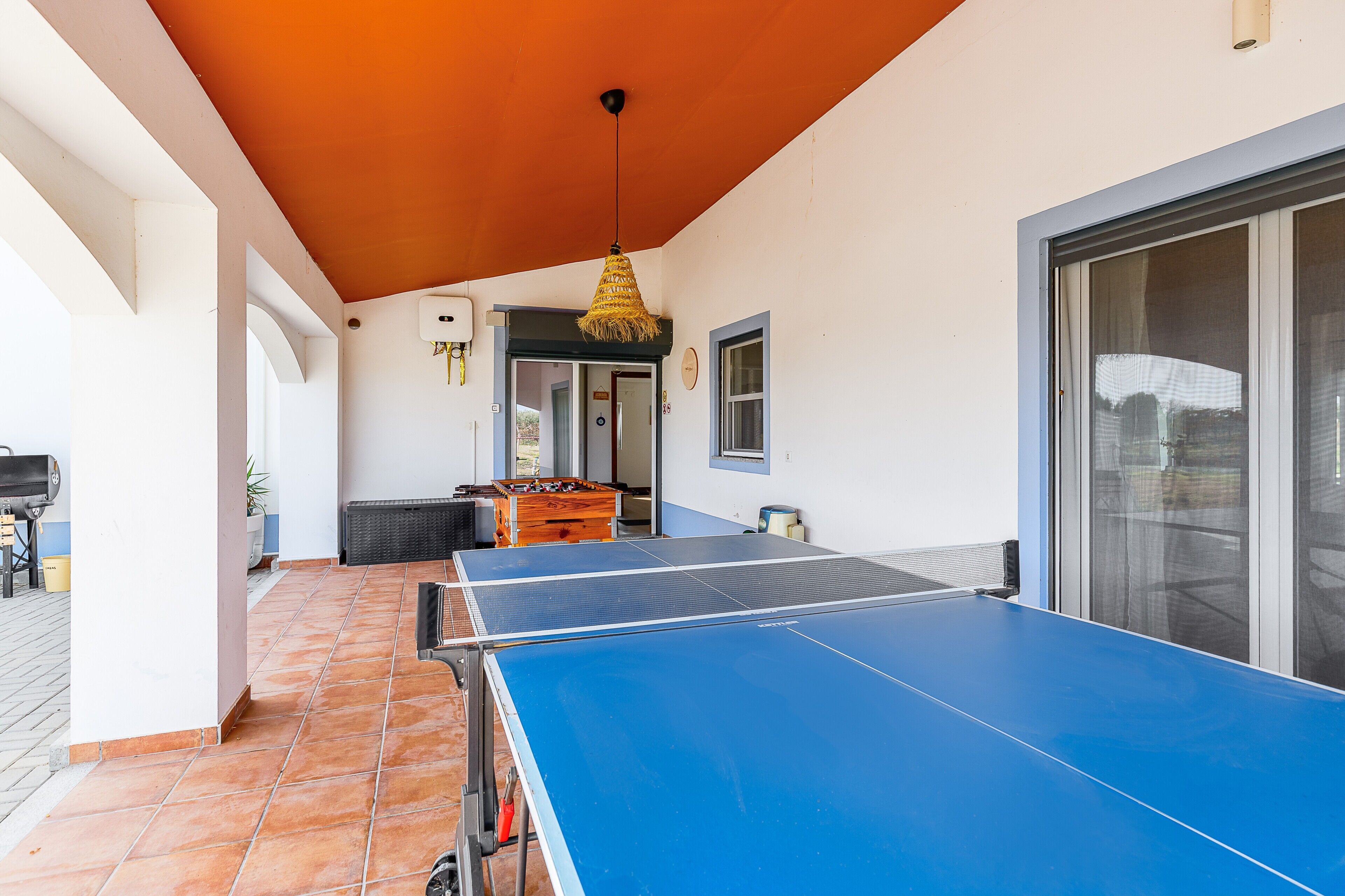 A ping pong table, a grill, and a dining table in a covered outdoor area.