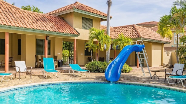 A pool area with a blue slide, lounge chairs, and a building with a tiled roof.
