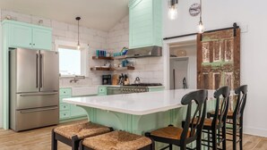A modern kitchen with a central island, stainless steel appliances, and a rustic wooden door. - New Listing "Somewhere at Sunset", 3 Bedrooms, 2 Baths, Waterfront, Sleeps 10 (Dauphin Island)