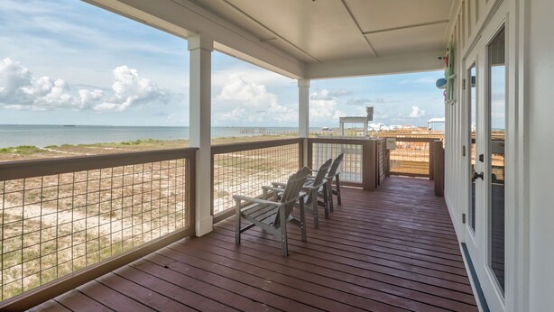 A covered porch with a view of the beach and ocean, featuring a railing, wooden deck, and a table with chairs. - New Listing "Somewhere at Sunset", 3 Bedrooms, 2 Baths, Waterfront, Sleeps 10 (Dauphin Island)