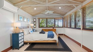 Ein Schlafzimmer mit einem Bett, Nachttischen, einem Deckenventilator und Fenstern mit Jalousien.