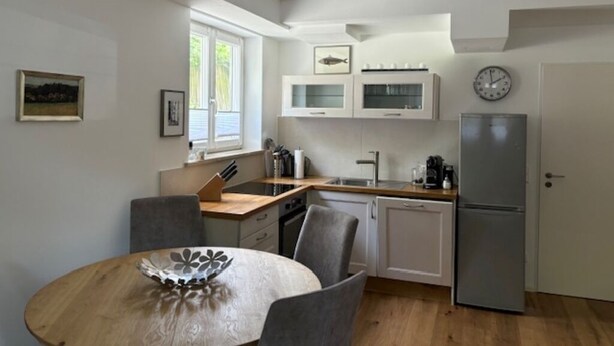 A compact kitchen with a dining table, chairs, a refrigerator, and a window providing natural light. - Apartment in the best location in Munich (München)