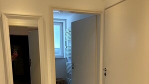 A hallway with a tiled floor, white walls, and a door leading to a room with a radiator and a window. - Apartment in the best location in Munich (München)