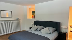 A modern bedroom with a bed, bedside tables, a radiator, and a framed picture on the wall. - Apartment in the best location in Munich (München)
