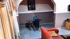 Un salon avec un canapé rouge, une petite table et un téléviseur. Il y a un tableau au mur et un rideau à gauche.