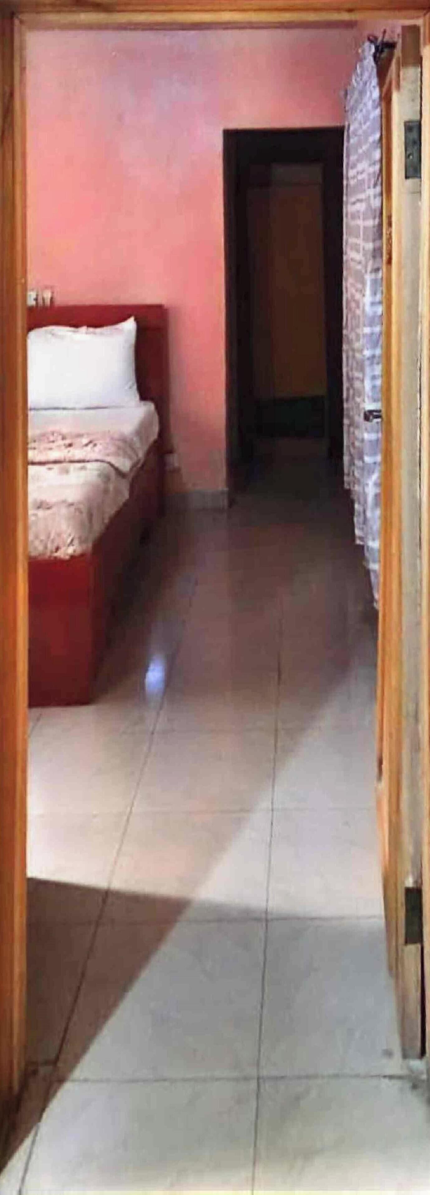Un pasillo estrecho con una cama a la izquierda y una puerta al final.