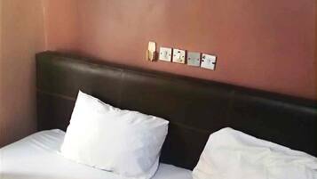 A hotel room with a single bed, white bedding, a dark headboard, and a wall-mounted light fixture.