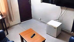 Une petite pièce avec une table en bois, un téléviseur fixé au mur, un petit meuble blanc et une porte.