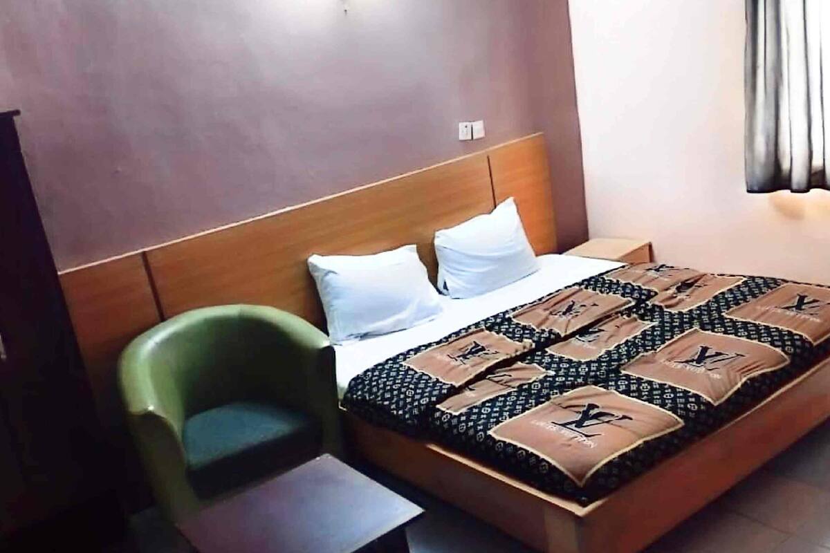 Quarto de hotel com cama, duas almofadas, uma cadeira verde e uma mesa pequena.