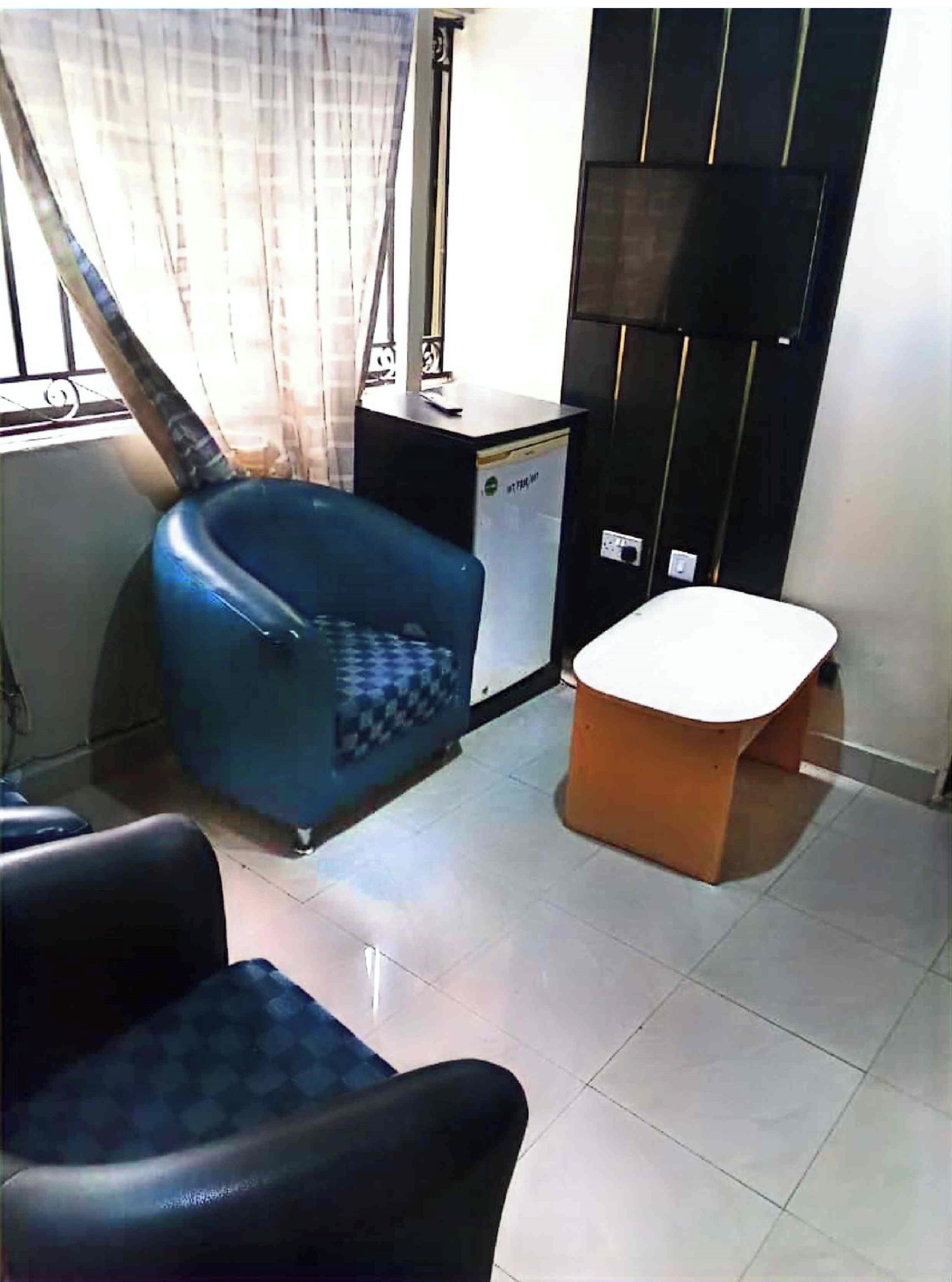 Una habitación con un sillón azul, una mesita blanca y un armario negro.