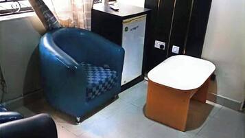 Una habitación con un sillón azul, una mesita blanca y un armario negro.