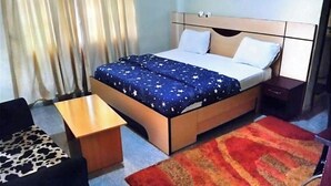 Une chambre d’hôtel avec un lit, une petite table, une chaise et un tapis rouge et orange.