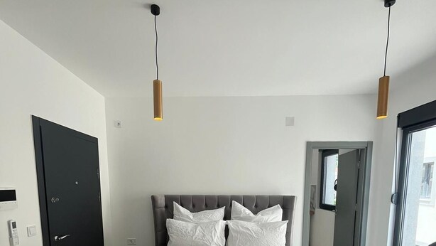 Ein modernes Schlafzimmer mit einem großen Bett, zwei Pendelleuchten, einer schwarzen Tür und Blick durch eine Glastür.