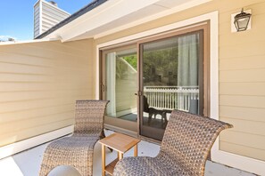 A covered patio with two wicker chairs and a small table, a sliding glass door, and a white fence visible through the door.