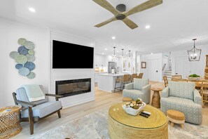 Un salon moderne avec une cheminée, un coin salon et une cuisine en arrière-plan.