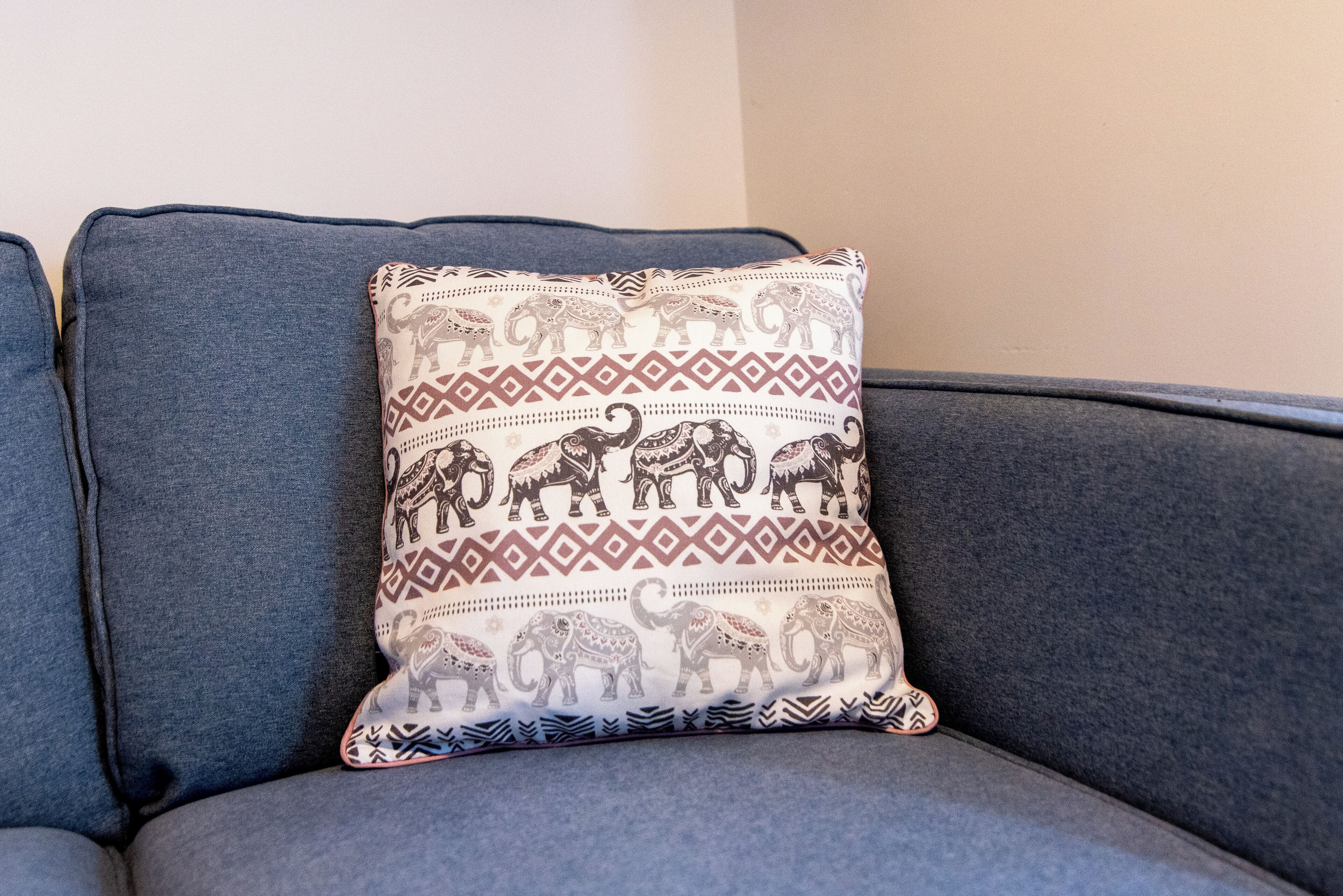 A grey sofa with a patterned cushion featuring elephant designs.