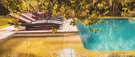 A swimming pool with a sunlit deck area, surrounded by trees.