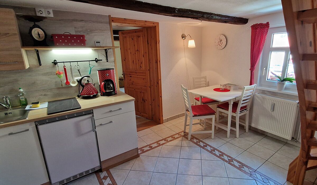 Una cocina compacta con puerta de madera, una mesa de comedor con sillas rojas y una ventana con cortina roja.