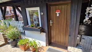 A wooden door with a mushroom-shaped welcome sign, potted plants, and a small window with a dreamcatcher decoration. - Ferienwohnung Fliegenpilz - 50m² OG1 (Quedlinburg)