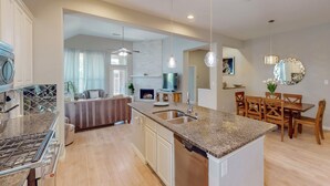 Una cocina moderna con encimeras de granito, estufa integrada y una zona de comedor con sillas y mesa de madera.