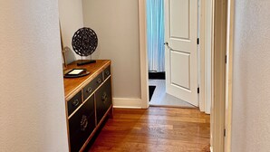 Een gang met houten vloer, een houten dressoir en een witte deur naar een andere kamer.
