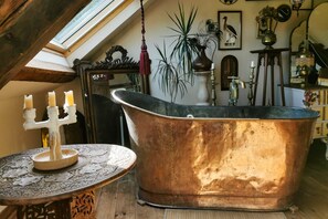 Une pièce dotée d’une grande baignoire en cuivre, d’une table avec un chandelier et de divers objets décoratifs.