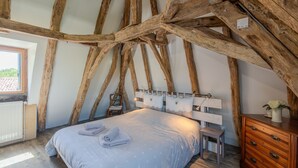 A bedroom with exposed wooden beams, a bed with towels, a chair, a dresser, and a window with a view. - Villa Le Bos - Three Bedroom Villa, Sleeps 6 (Pezuls)