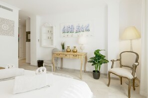 A bedroom with a bed, a desk with a lamp, a chair, and a potted plant.