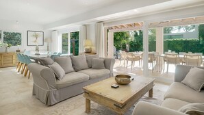Ein geräumiges Wohnzimmer mit einem beigefarbenen Sofa, einem Holztisch und einem Essbereich mit weißen Stühlen.
