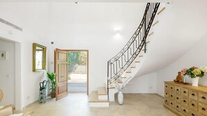 Ein geräumiger Raum mit einer geschwungenen Treppe, einem Holzkabinett und einem Sessel.
