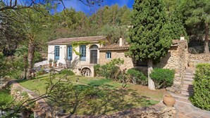 A stone house with a tiled roof, surrounded by greenery and a stone wall.