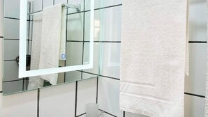 A bathroom with a glass shower enclosure, a white towel hanging on a rack, and a mirror reflecting the bathroom. - 1 Bed Studio Sleeps 2 - Canal View, Wifi, Parking (Douala)