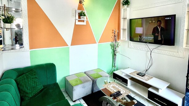 A living room with a green sofa, a coffee table, and a TV mounted on the wall. - 1 Bed Studio Sleeps 2 - Canal View, Wifi, Parking (Douala)