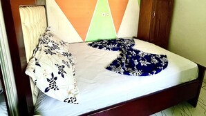 A neatly made bed with a floral-patterned blanket, a wooden headboard, and a geometric-patterned wall hanging above it. - 1 Bed Studio Sleeps 2 - Canal View, Wifi, Parking (Douala)
