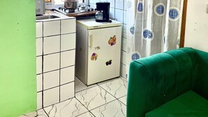A compact kitchen with a refrigerator, stove, and sink. A green sofa is in the foreground. - 1 Bed Studio Sleeps 2 - Canal View, Wifi, Parking (Douala)
