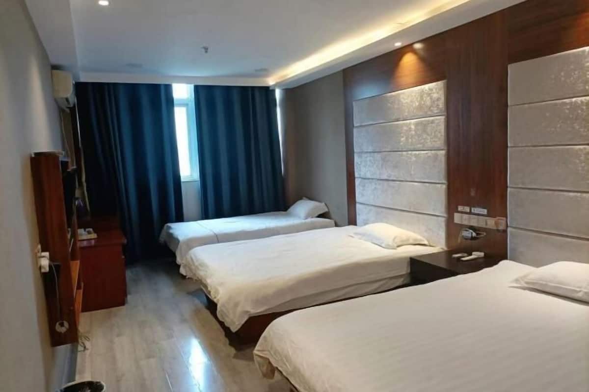 Een hotelkamer met twee bedden, een houten hoofdeinde, een bureau en een raam met gordijnen.