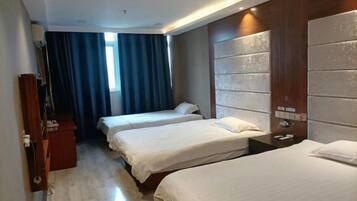 A hotel room with two beds, a wooden headboard, a desk, and a window with curtains.