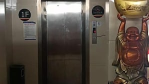 An elevator with a sign indicating floor 1F, a trash bin, and a statue of a seated figure holding a bowl.