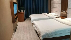 A hotel room with two beds, a TV, a desk, and a plant.
