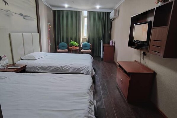 Ein Hotelzimmer mit zwei Betten, einem Schreibtisch, einem Sessel, einem Fernseher und einem kleinen Tisch mit einer Pflanze.