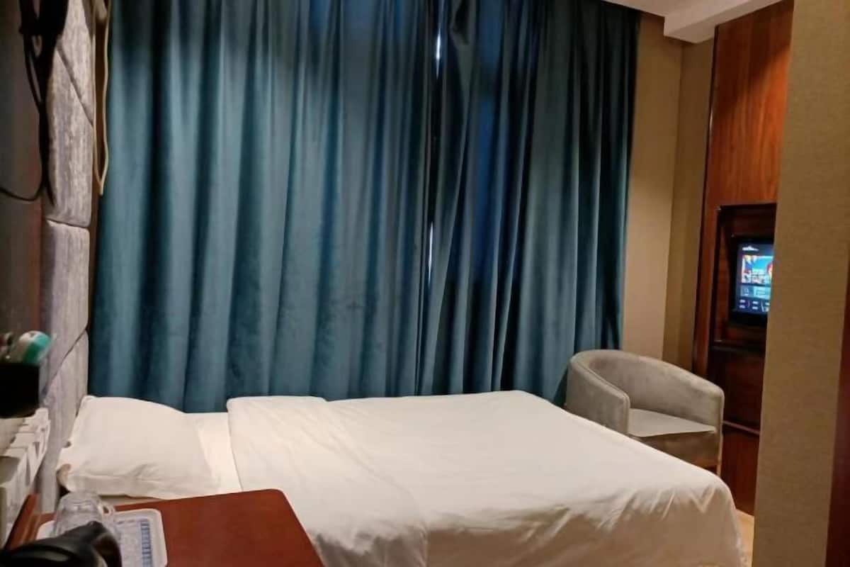 Een hotelkamer met een bed, een stoel, een televisie en een gordijn.