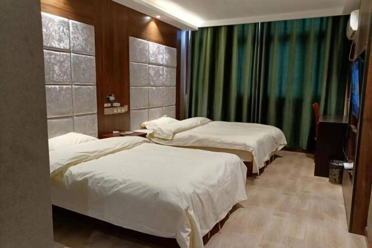 Een hotelkamer met twee bedden, een grote spiegel, een houten hoofdbord en een groen gordijn.