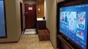 A hotel hallway with a wooden floor, a reception desk, and a television displaying various programs.
