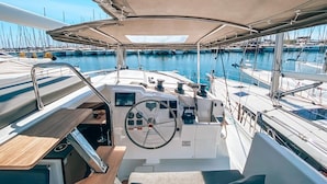 A boat deck with a steering wheel, control panels, and a dining area.