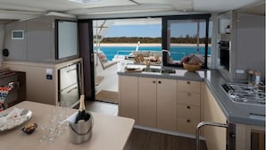 A yacht's interior with a dining area, kitchen, and a view of the sea.