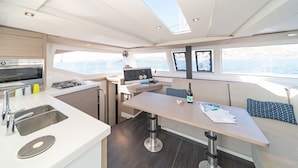 A compact kitchen with a microwave, stove, and sink, a dining area with a table and chairs, and large windows offering a view of the sea.