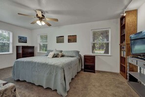Un dormitorio con una cama, ventilador de techo, televisor y estantería.