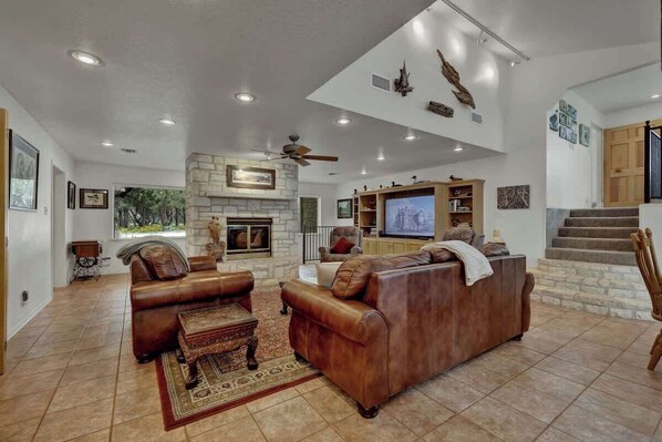 Amplia sala de estar con sofás de cuero, chimenea, televisor y escalera.