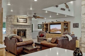 Amplia sala de estar con sofás de cuero, chimenea de piedra, televisor de pantalla plana y ventilador de techo.